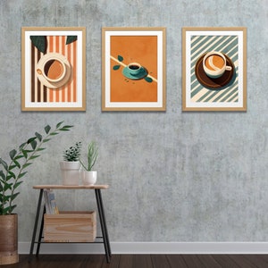 May include: Three framed prints of coffee cups on different backgrounds. The first print has a striped background with a brown and white coffee cup. The second print has an orange background with a green coffee cup. The third print has a blue and white striped background with a brown coffee cup.