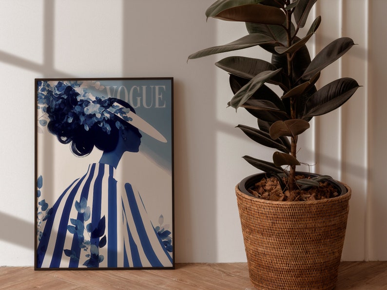 May include: A framed print of a blue and white illustration of a woman wearing a hat with the word "VOGUE" printed on the top of the frame.
