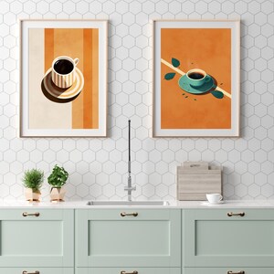 Puede incluir: Dos ilustraciones enmarcadas de tazas de caf&eacute; en una pared de azulejos blancos. Las ilustraciones son de estilo retro con fondos naranja y amarillo. La primera ilustraci&oacute;n muestra una taza de caf&eacute; con un platillo sobre un fondo a rayas naranja y amarillo. La segunda ilustraci&oacute;n muestra una taza de caf&eacute; con un platillo sobre un fondo naranja con una hoja verde.