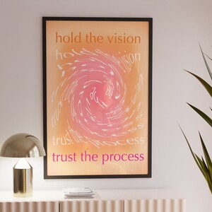 以下が含まれることがあります： ピンクとオレンジの渦巻き模様のモチベーションポスター。"hold the vision trust the process"というテキストが白とピンクで書かれています。