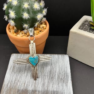 May include: A silver pendant with a turquoise heart in the center, surrounded by four silver bars. The pendant is in the shape of a cross.