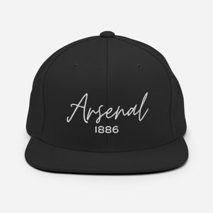 May include: Black and white embroidered baseball cap with the text "Arsenal 1886" in a cursive font.