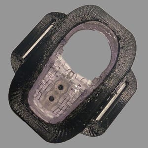 Op de afbeelding: Een zwarte plastic ring met een transparante plastic inzet. De inzet heeft een printplaatontwerp met twee kleine zwarte cirkels.