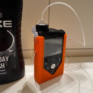 May include: An orange and black medical device with a clear tube attached. The device has a screen and several buttons. A black bottle of body wash is to the left of the device.