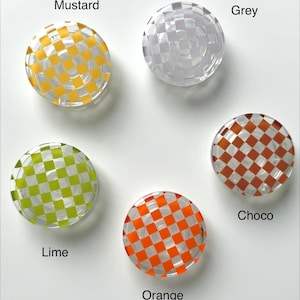May include: Five round, clear glass objects with a checkered pattern in mustard yellow, grey, lime green, orange, and chocolate brown. Each object has a different color and is labeled with its respective color name.