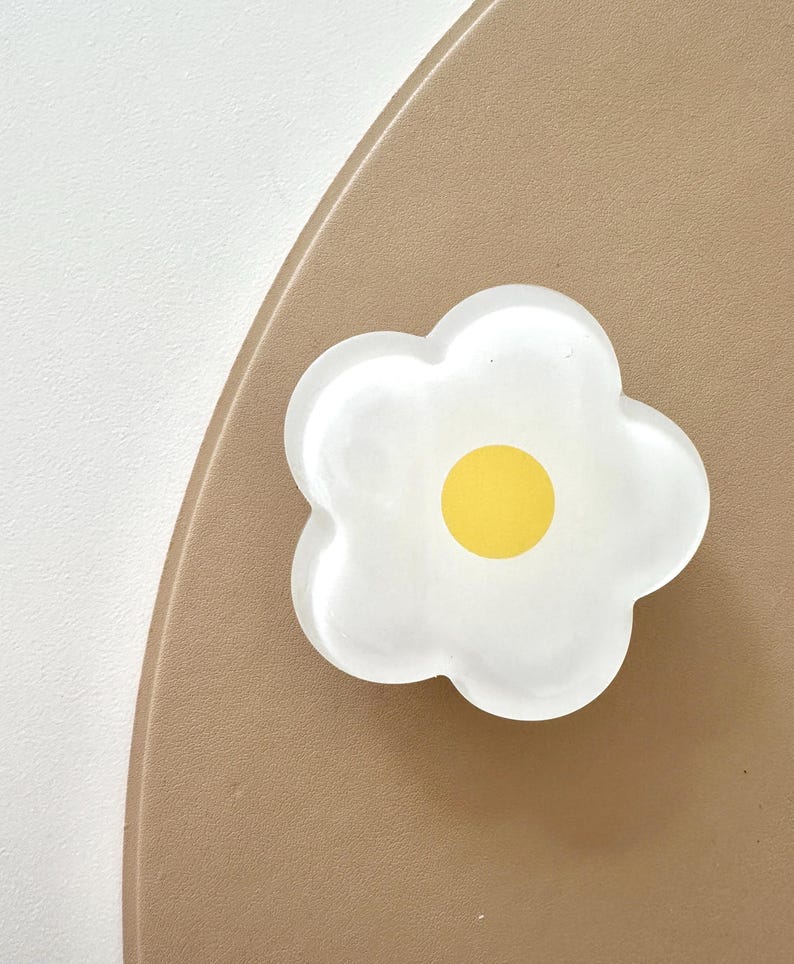 Op de afbeelding: Een witte, bloemvormige harsknop met een geel centrum. De knop bevindt zich op een bruine achtergrond.