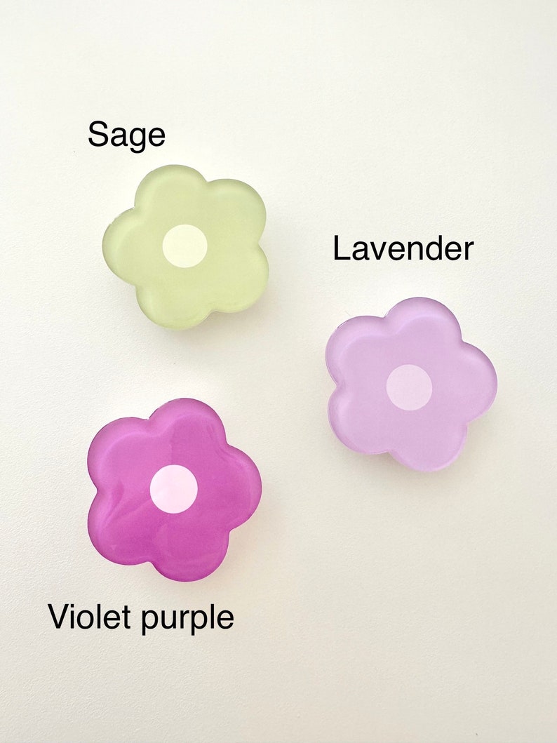 Op de afbeelding: Drie haarclips in de vorm van bloemen gemaakt van hars in de kleuren saliegroen, lavendel en violet.
