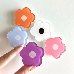 Op de afbeelding: Vijf kleurrijke, bloemvormige telefoonbeugels van hars met witte centra. De bloemen zijn in tinten oranje, wit, lichtblauw, roze en paars.