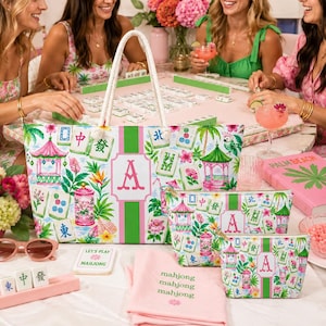 May include: A set of mahjong-themed accessories, including a tote bag, cosmetic bags, and a pink towel. The items feature a floral and pagoda design with the letter "A". The scene includes a mahjong game in progress.