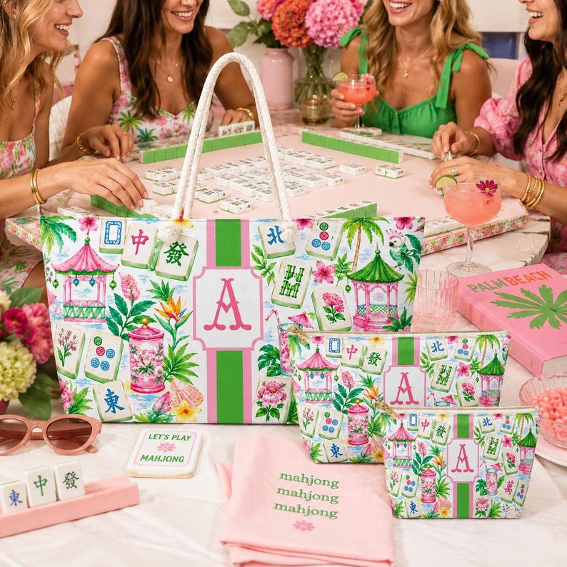 May include: A set of mahjong-themed accessories, including a tote bag, cosmetic bags, and a pink towel. The items feature a floral and pagoda design with the letter "A". The scene includes a mahjong game in progress.