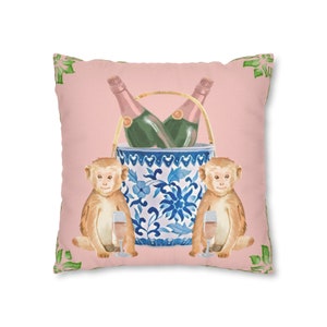 May include: A pink throw pillow with a blue and white porcelain bucket with two champagne bottles inside. Two monkeys are on either side of the bucket, each holding a glass of champagne.