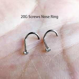 May include: Two silver nose rings with clear gem stones. The nose rings are 20 gauge and have a screw-on design.