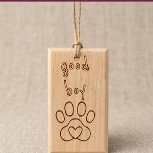 May include: Wooden car air freshener with the words "good boy" and a paw print design. The rectangular block is made of light-colored wood and has a jute string for hanging. The text "DIY CAR AIR FRESHENER" is at the top.