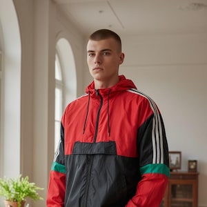 May include: A red, black, and white hooded jacket with a zip. The jacket has white stripes on the sleeves and a green accent. The person is wearing dark blue jeans. The jacket is a sporty, casual style.