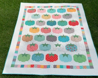 May include: A white quilt with a blue border and a pattern of colorful tomato shapes. The quilt is made with a variety of fabrics and textures.