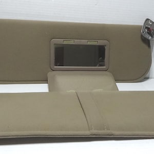 Può includere: Due parasole per auto color beige con fissaggi in metallo. Un parasole ha uno specchio integrato. I parasole sono realizzati in un materiale morbido e imbottito. L'immagine mostra due parasole.