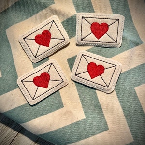 May include: Four white felt patches with red embroidered hearts inside a black outline of an envelope. The patches are on a white and blue chevron fabric.