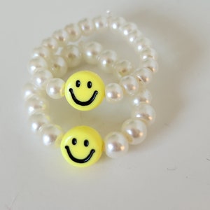 May include: Two white pearl bracelets with yellow smiley face charms.