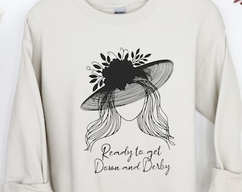 May include: A cream-colored sweatshirt with a black graphic of a woman wearing a large hat with flowers and the text "Ready to get Down and Derby".