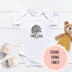 May include: White baby onesie with a black and white tree logo that says "EST. YOUR LOGO HERE SO."  The onesie is on a white wooden surface with a brown teddy bear and two pairs of beige baby shoes.