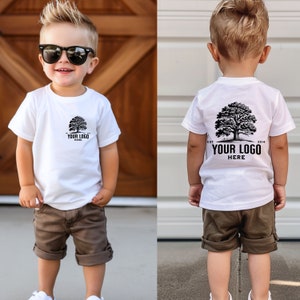 May include: A white t-shirt with a black tree and the text "EST. 2014 YOUR LOGO HERE" on the back. The shirt is being worn by a young child wearing brown shorts.