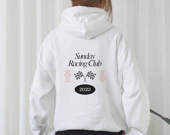 Puede incluir: Sudadera con capucha blanca con el texto "Sunday Racing Club" y un gráfico de bandera a cuadros en la espalda. El año 2022 está impreso debajo del gráfico.
