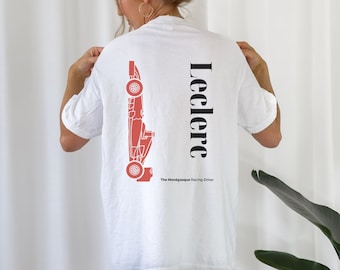 Puede incluir: Camiseta blanca con un gráfico de coche de carreras rojo y el texto "Leclerc The Monagasque Racing Driver" en la espalda.
