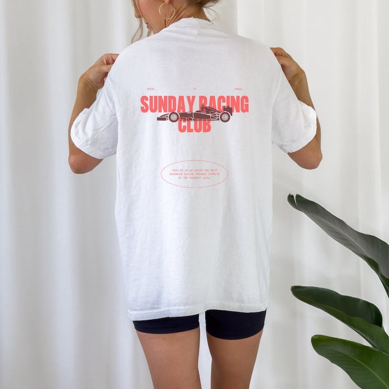 May include: White t-shirt with a red graphic of a race car and the text "SUNDAY RACING CLUB". The text "WHEEL TO WHEEL" is printed above the graphic and the text "JOIN US AS WE WRITE THE NEXT CHAPTER OF RACING HISTORY, ONE LAP AT THE PERFECT LEVEL" is printed below the graphic.