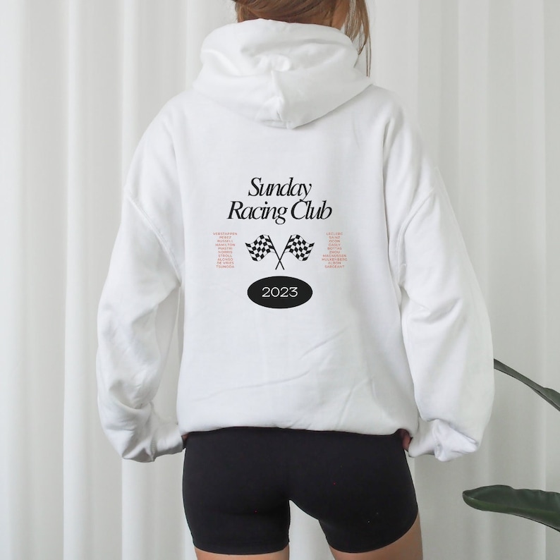 Puede incluir: Sudadera con capucha blanca con el texto "Sunday Racing Club" y un gr&aacute;fico de bandera a cuadros. El a&ntilde;o 2023 est&aacute; impreso en un c&iacute;rculo debajo del gr&aacute;fico.