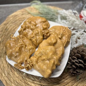 May include: A white plate with six pecan pralines, each with a walnut inside, on a woven straw placemat.