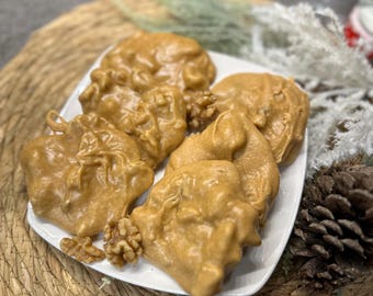 Peut inclure: Une assiette blanche avec six pralines aux noix de pécan, chacune contenant une noix, sur un dessous de plat en paille tressée.