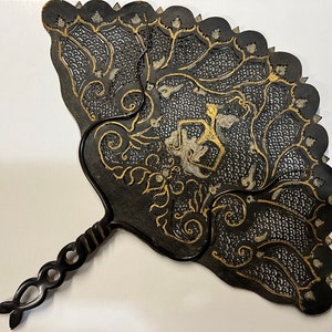 May include: A black hand fan with intricate gold and silver designs. The fan is made of a thin, flexible material and has a long, black handle.