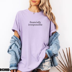 May include: A light purple t-shirt with the text "financially irresponsible" printed on the front.