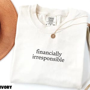 May include: Ivory t-shirt with the text "financially irresponsible" printed in black.