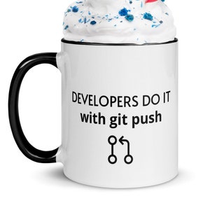 Może przedstawiać: Biały kubek ceramiczny z czarnym uchwytem. Kubek ma czarną obwódkę i napis "DEVELOPERS DO IT with git push" oraz grafikę symbolu scalania kodu. Kubek jest wypełniony bitą śmietaną i niebieskimi posypkami i ma czerwoną i białą słomkę w paski.