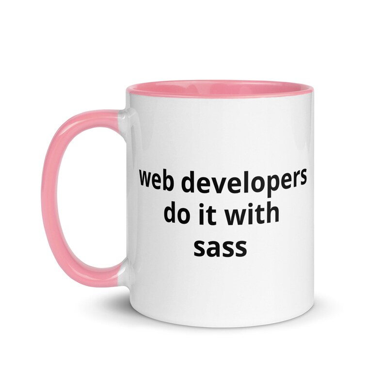 K&ouml;nnte beinhalten: Eine wei&szlig;e Keramiktasse mit rosafarbenem Rand und Henkel. Die Tasse hat einen schwarzen Schriftzug mit der Aufschrift "web developers do it with sass".