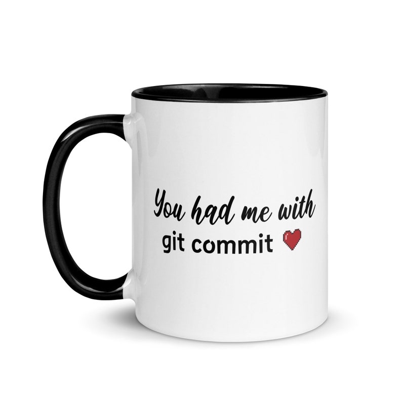Op de afbeelding: Witte koffiemok met een zwarte rand en handvat. De mok heeft de tekst "You had me with git commit" en een rood gepixelde hart.