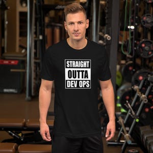 May include: Black t-shirt with the text "STRAIGHT OUTTA DEV OPS" in a white, rectangular design. The shirt is worn by a person in a gym setting.