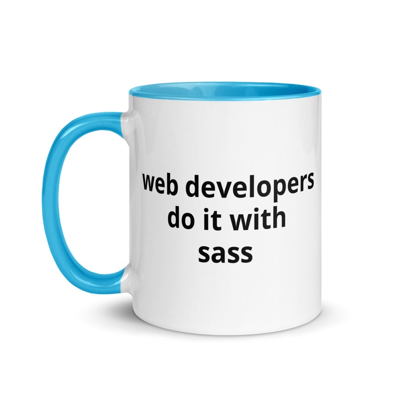K&ouml;nnte beinhalten: Eine wei&szlig;e Keramiktasse mit blauem Rand und Henkel. Die Tasse hat einen schwarzen Text mit der Aufschrift "web developers do it with sass".