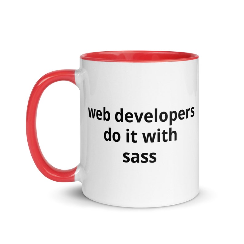 K&ouml;nnte beinhalten: Eine wei&szlig;e Keramiktasse mit rotem Rand und Henkel. Die Tasse hat einen schwarzen Text mit der Aufschrift "web developers do it with sass".