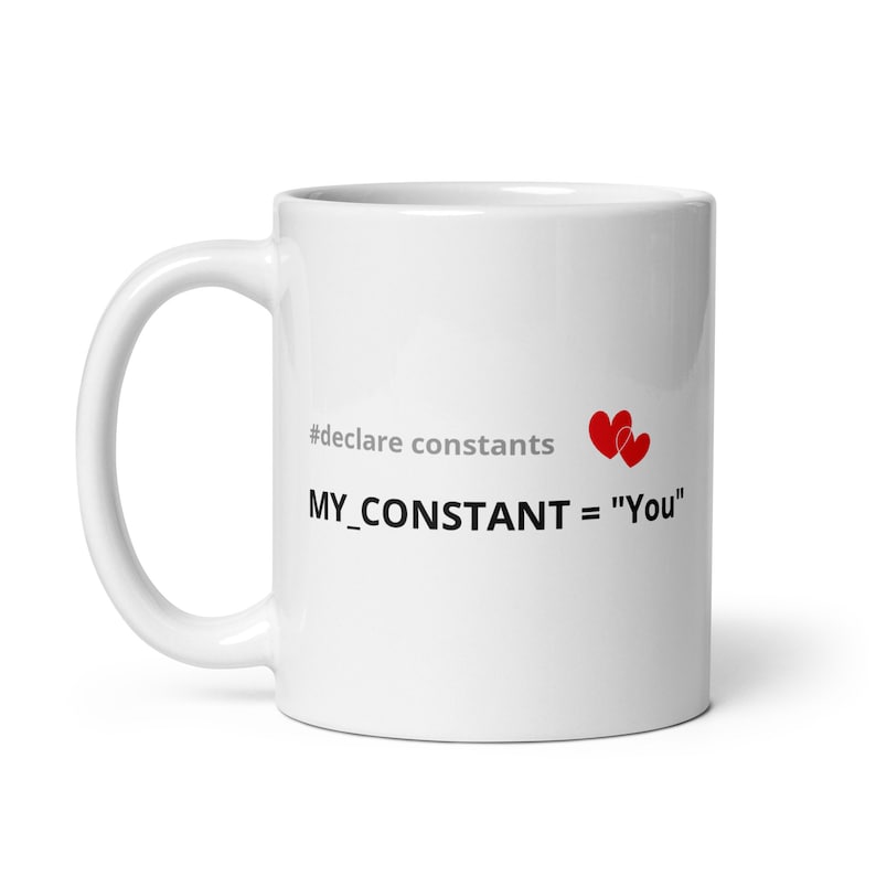 May include: White ceramic mug with black text that reads "#declare constants MY_CONSTANT = "You"" with two red hearts above the text.