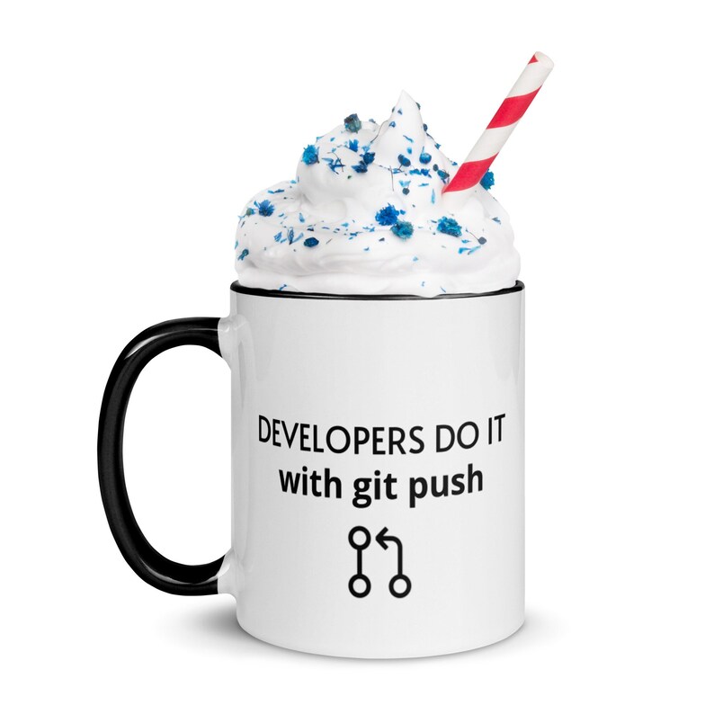 Peut inclure: Une tasse en c&eacute;ramique blanche avec une anse noire. La tasse a un bord noir et le texte "DEVELOPERS DO IT with git push" et un graphique d'un symbole de fusion de code. La tasse est remplie de cr&egrave;me fouett&eacute;e et de p&eacute;pites bleues et a une paille ray&eacute;e rouge et blanche.