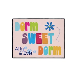 May include: A pink doormat with the text "Dorm Sweet Dorm" in colorful letters. The text "Ally & Evie" is below the main text with a blue flower graphic.