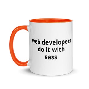 K&ouml;nnte beinhalten: Eine wei&szlig;e Kaffeetasse mit orangefarbenem Rand und Henkel. Die Tasse hat einen schwarzen Text mit der Aufschrift "web developers do it with sass".