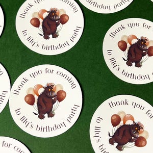 May include: White circular stickers with a brown cartoon creature holding balloons. The stickers say "Thank you for coming to Lily's birthday party" in a circular design. The background is a solid green.