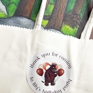 May include: A white paper gift bag with a circular sticker that reads "thank you for coming to lily's birthday party." The sticker features a cartoon monster holding balloons. The background shows a forest scene.