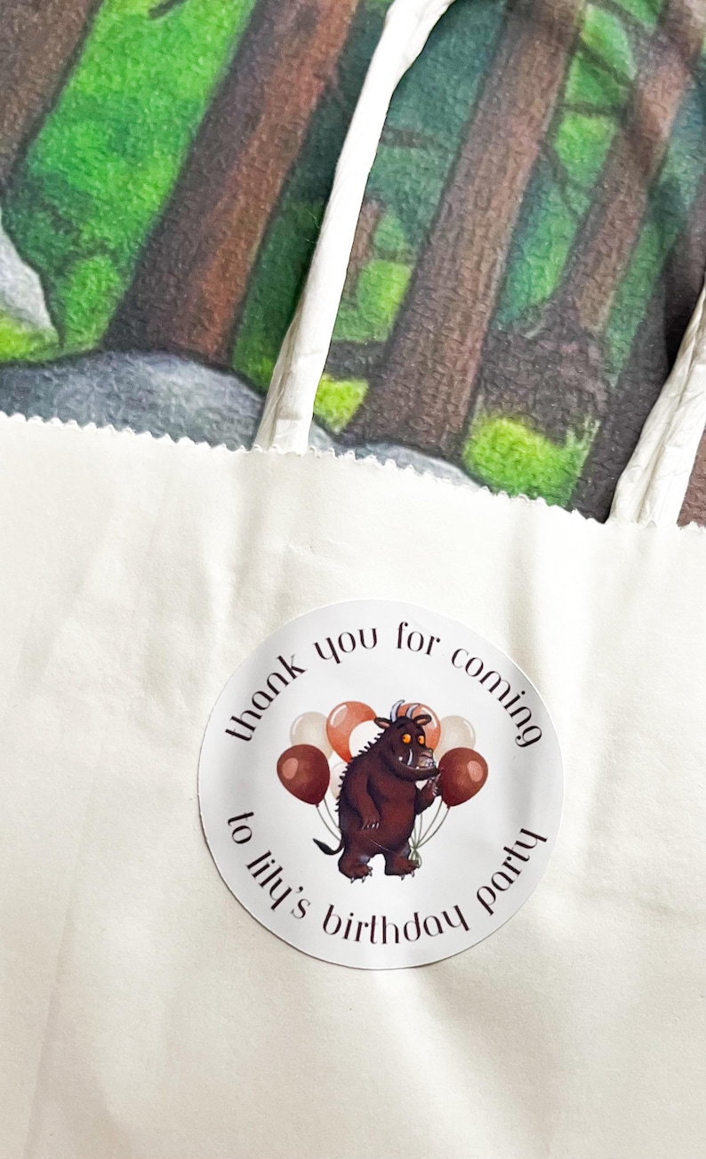 May include: A white paper gift bag with a circular sticker that reads "thank you for coming to lily's birthday party." The sticker features a cartoon monster holding balloons. The background shows a forest scene.