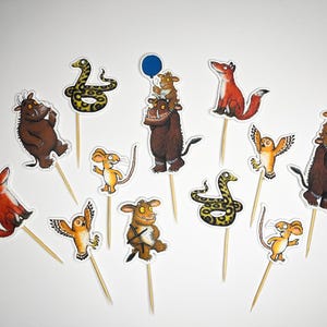 May include: A selection of colourful cupcake toppers featuring cartoon characters such as a fox, owl, snake, mouse, and a brown monster. Each character is attached to a wooden toothpick, ideal for decorating cakes and cupcakes.