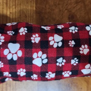 以下が含まれることがあります： 赤と黒のチェック柄で、白い足跡が特徴の長方形のペット用おもちゃ。ペット用にデザインされており、布製です。