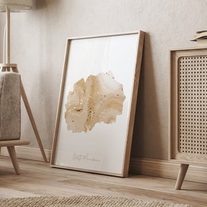 Könnte beinhalten: Ein gerahmter Druck eines Aquarells der Umrisse von Nordmazedonien in Gold- und Brauntönen. Der Druck hängt an einer beigefarbenen Wand in einem Wohnzimmer.